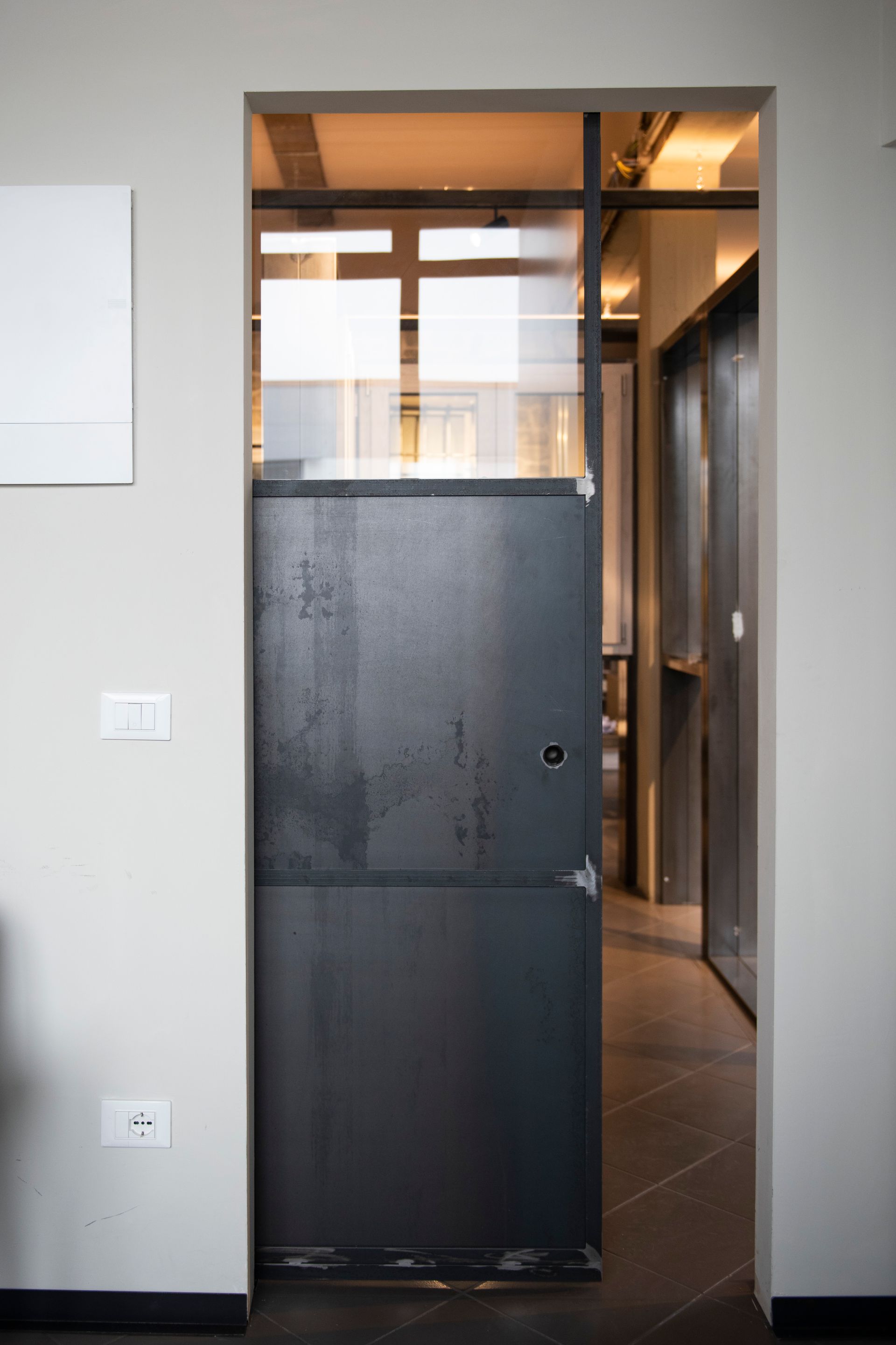 Porta in metallo scuro con pannelli in vetro, inserita in una parete di colore neutro.