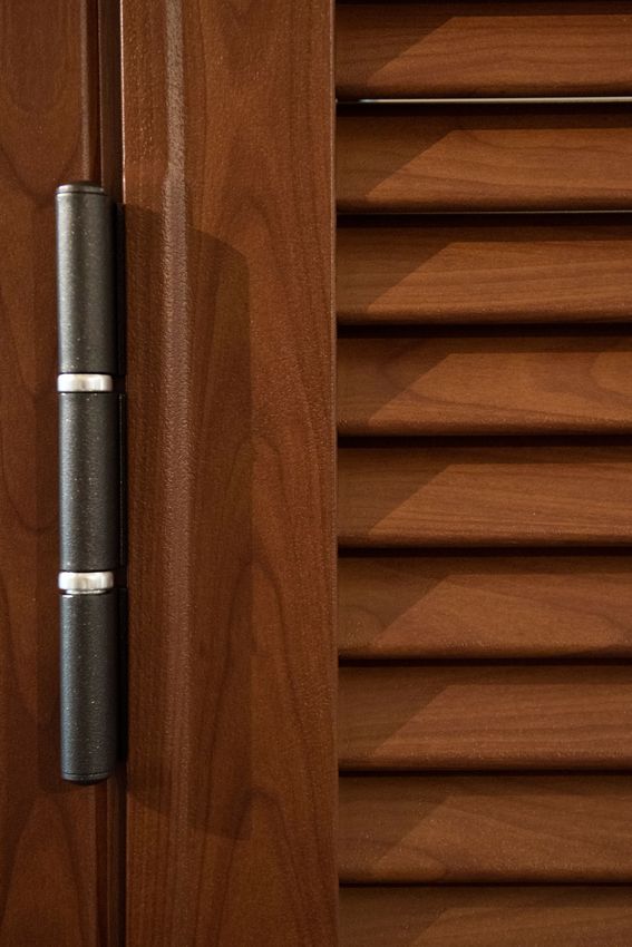 Porta in legno marrone scuro con cerniera in metallo scuro e persiane orizzontali.