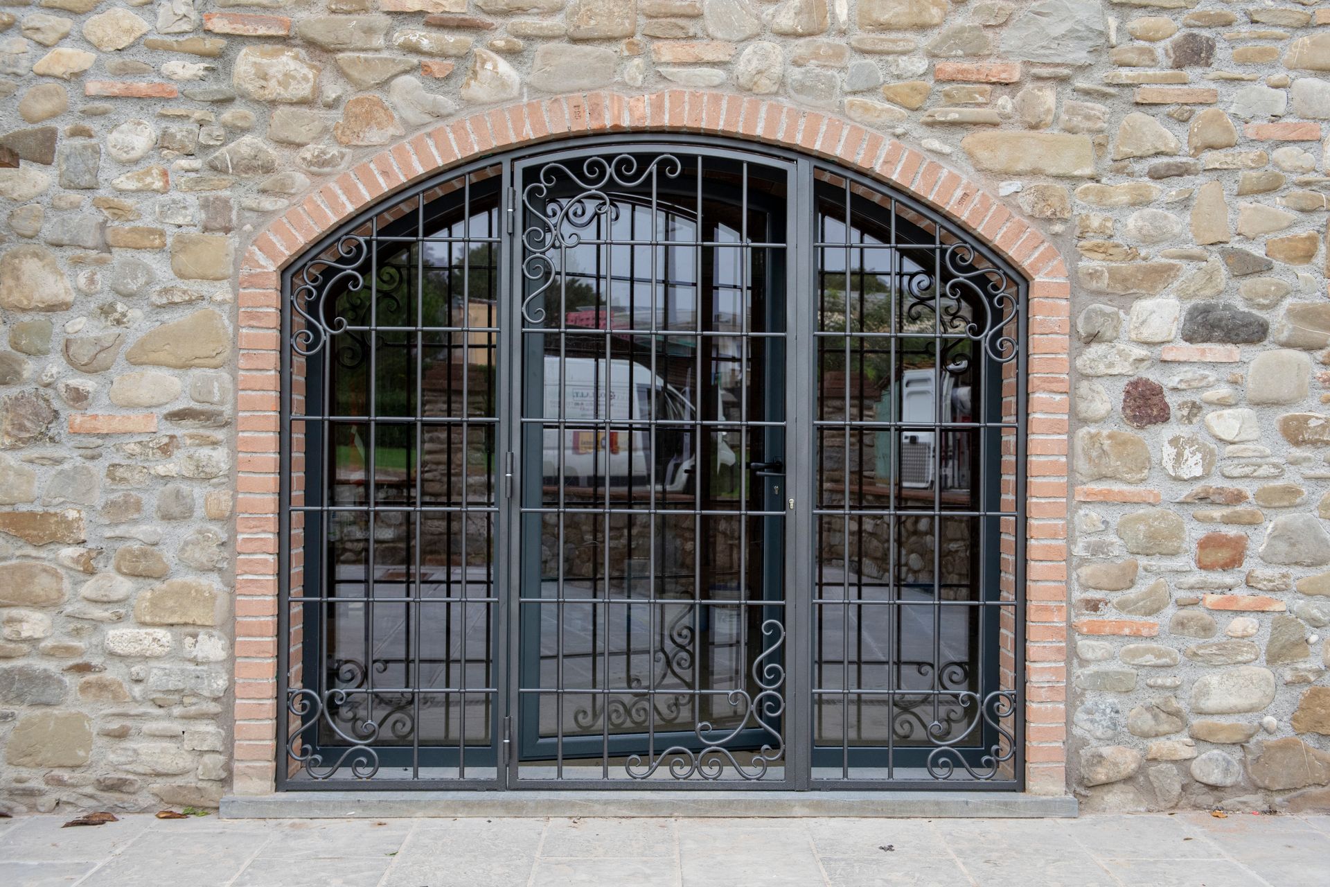 Porta ad arco con cancello decorativo in ferro in un muro di mattoni e pietra.