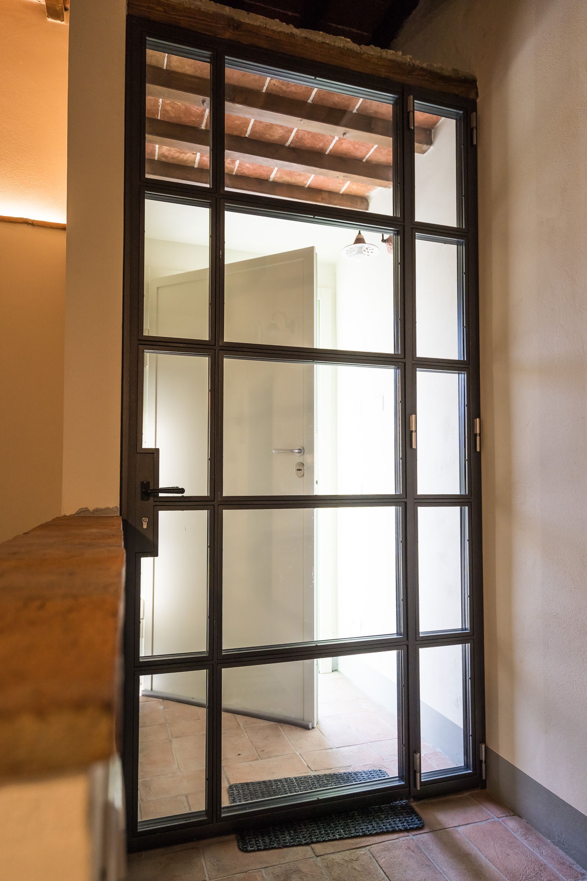 Porta di sicurezza in metallo con motivo a griglia, parzialmente aperta, montata sulla parete esterna.