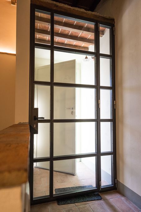Porta di sicurezza in metallo con motivo a griglia, parzialmente aperta, montata sulla parete esterna.