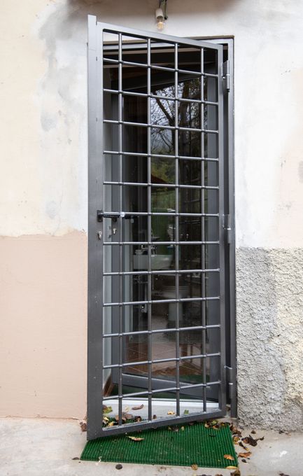 Porta di sicurezza in metallo con motivo a griglia, parzialmente aperta, montata sulla parete esterna.