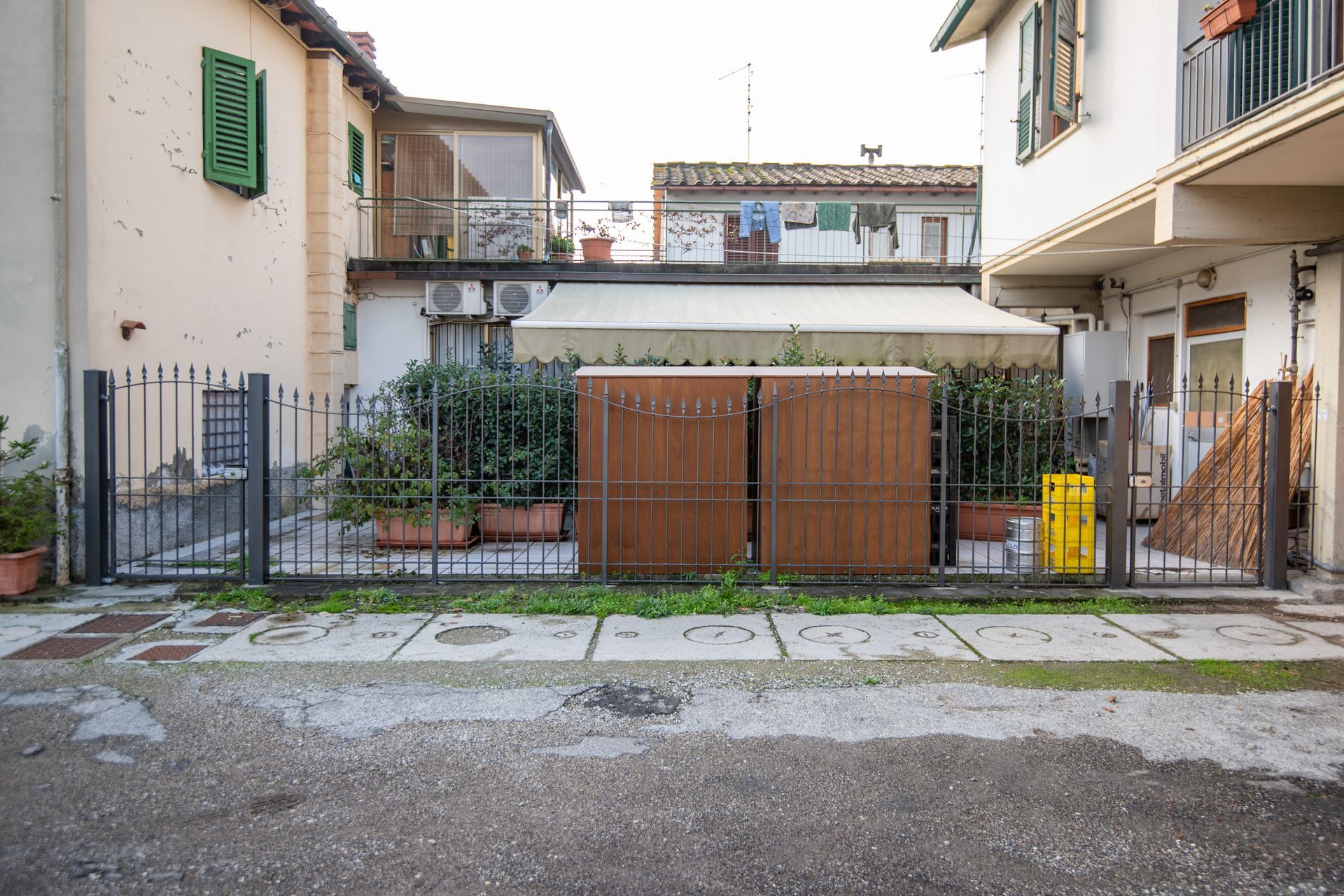 Edifici e un'area recintata con verde e porte in legno marrone su una strada acciottolata.