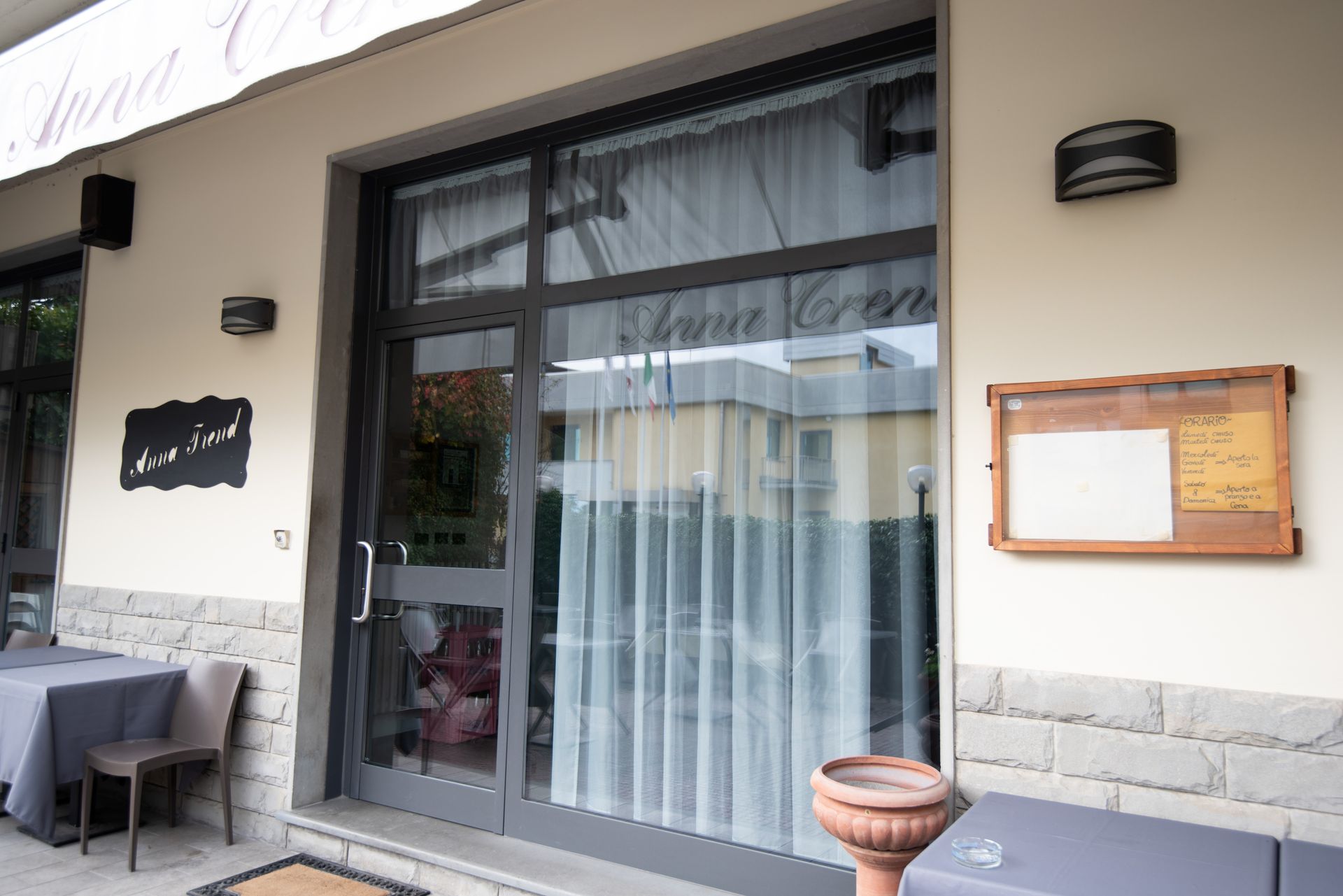 Esterno di un ristorante con una porta grigia, una tenda da sole e una piccola insegna.