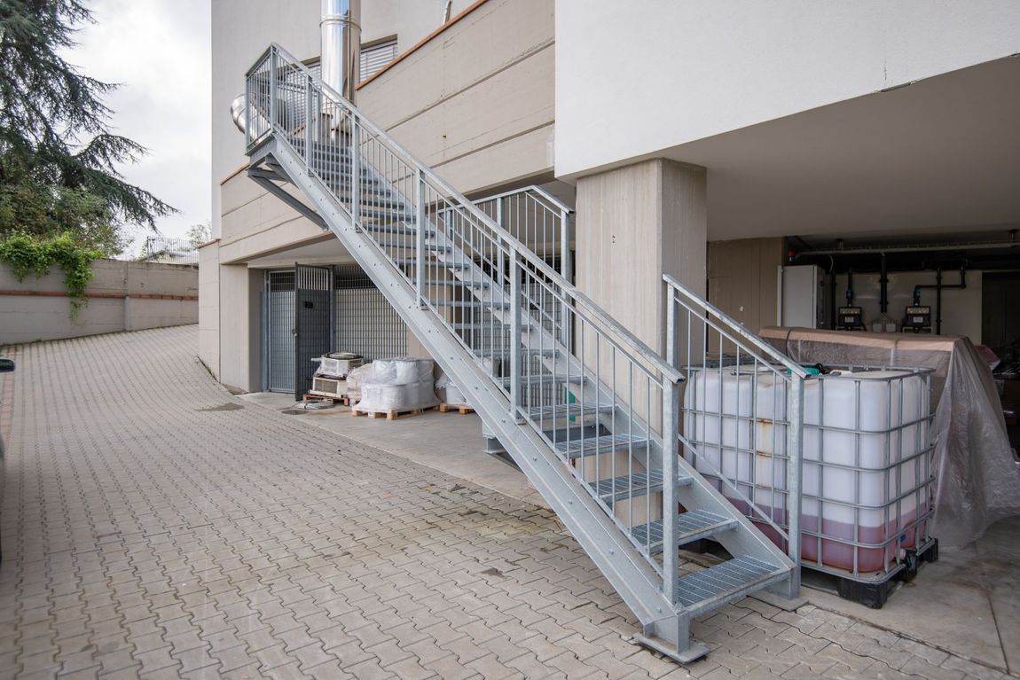 Scala esterna in metallo che conduce alla sommità di un edificio, con corrimano, su una superficie pavimentata.