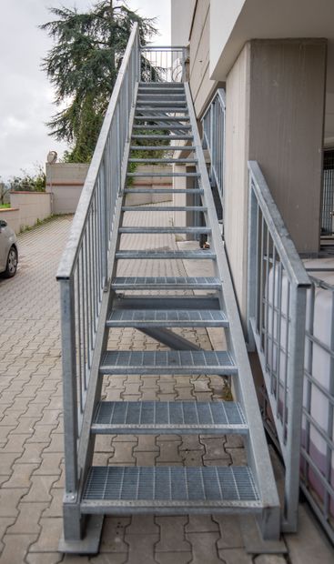 Scala in metallo contro l'esterno di un edificio. Gradini e corrimano in metallo grigio.