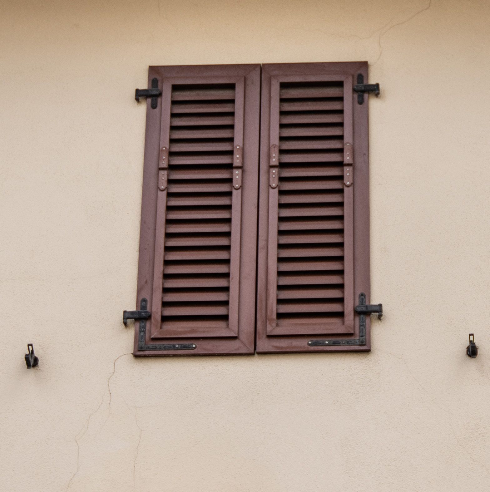 Persiane in legno marrone su una parete chiara con piccoli ganci metallici su entrambi i lati.
