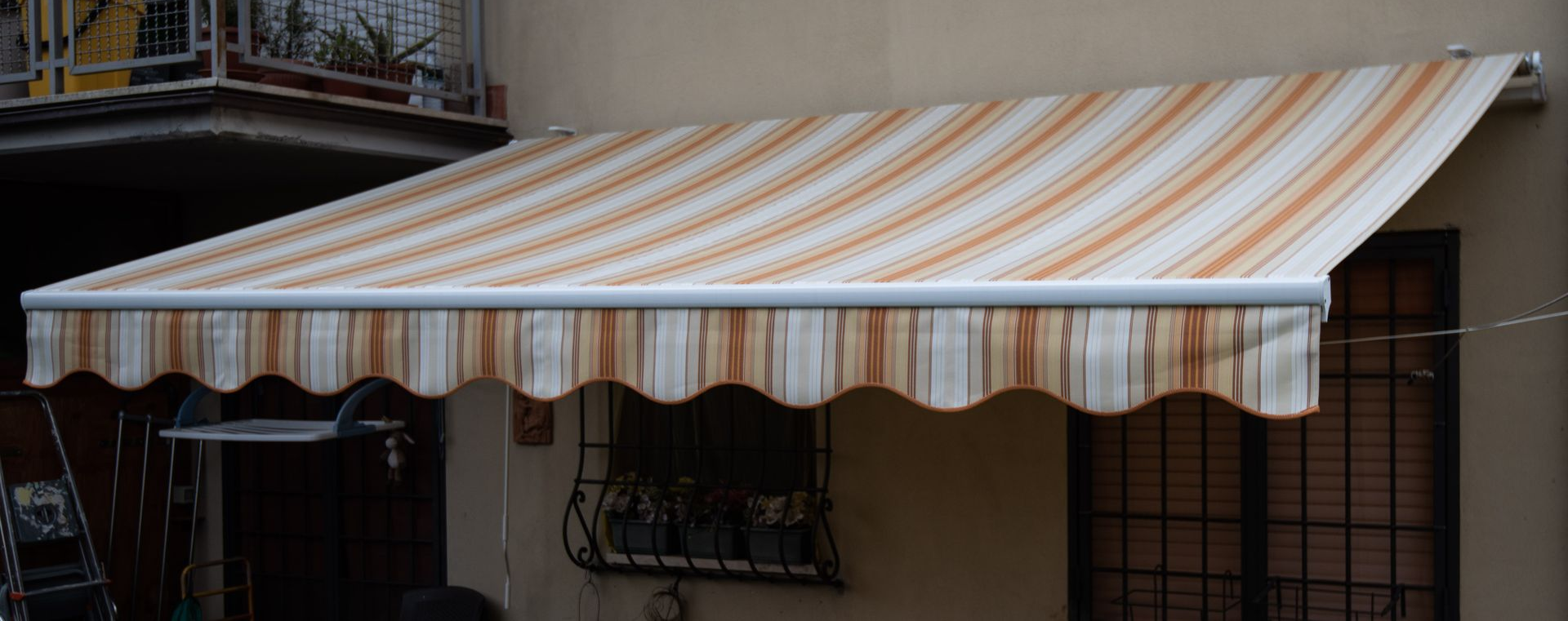 Tenda a strisce beige e marroni sopra una finestra, fissata all'esterno di un edificio.