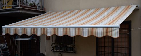 Tenda a strisce beige e marroni sopra una finestra, fissata all'esterno di un edificio.
