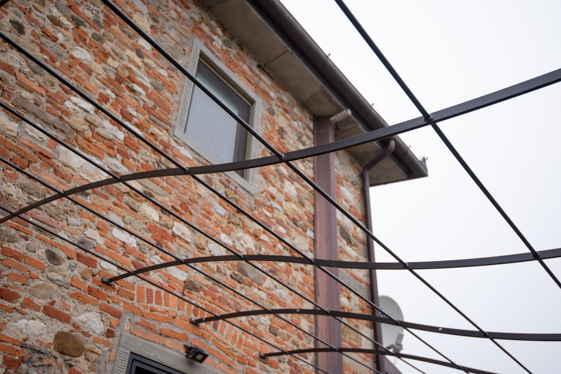 Esterno di un edificio in mattoni con traliccio metallico, finestra e cielo coperto.