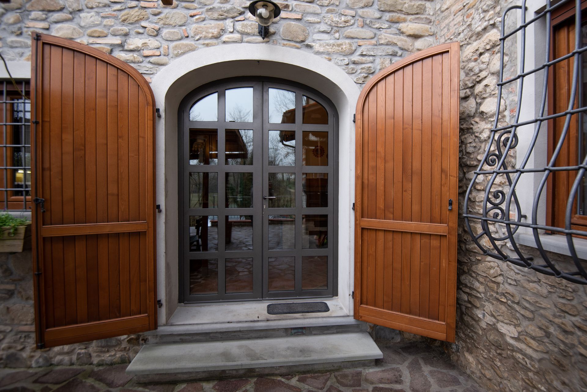 Porta di legno con persiane aperte, ingresso ad arco, muro di pietra.