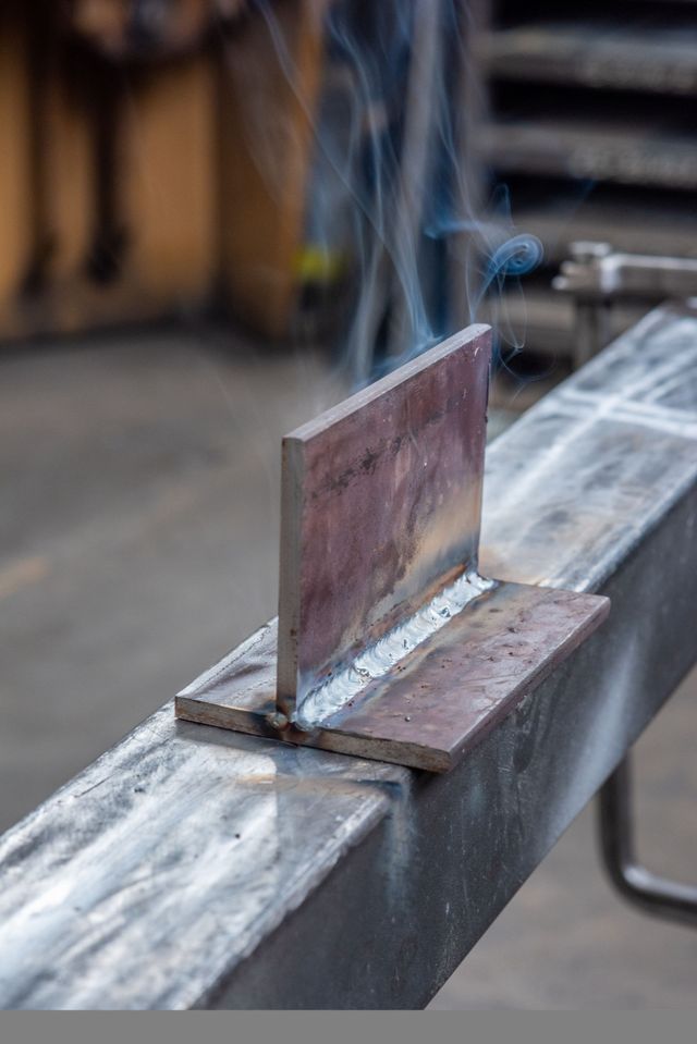 Lamiera saldata a una trave, dalla cui giunzione esce del fumo in un'officina.