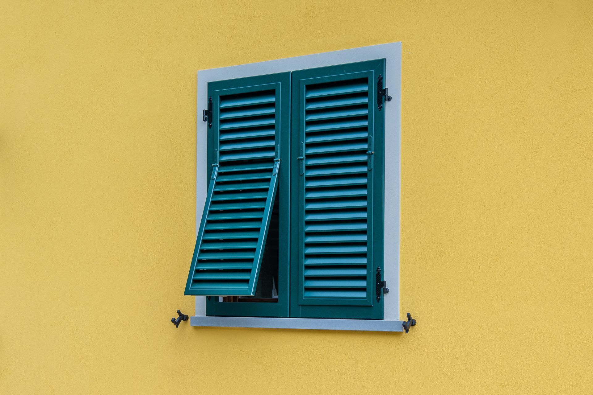 Persiane verdi su un muro giallo, una persiana aperta.