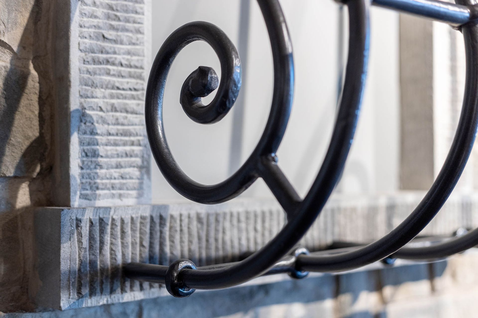 Primo piano di una ringhiera in ferro nero decorato con un motivo a spirale contro un muro in pietra ruvida.