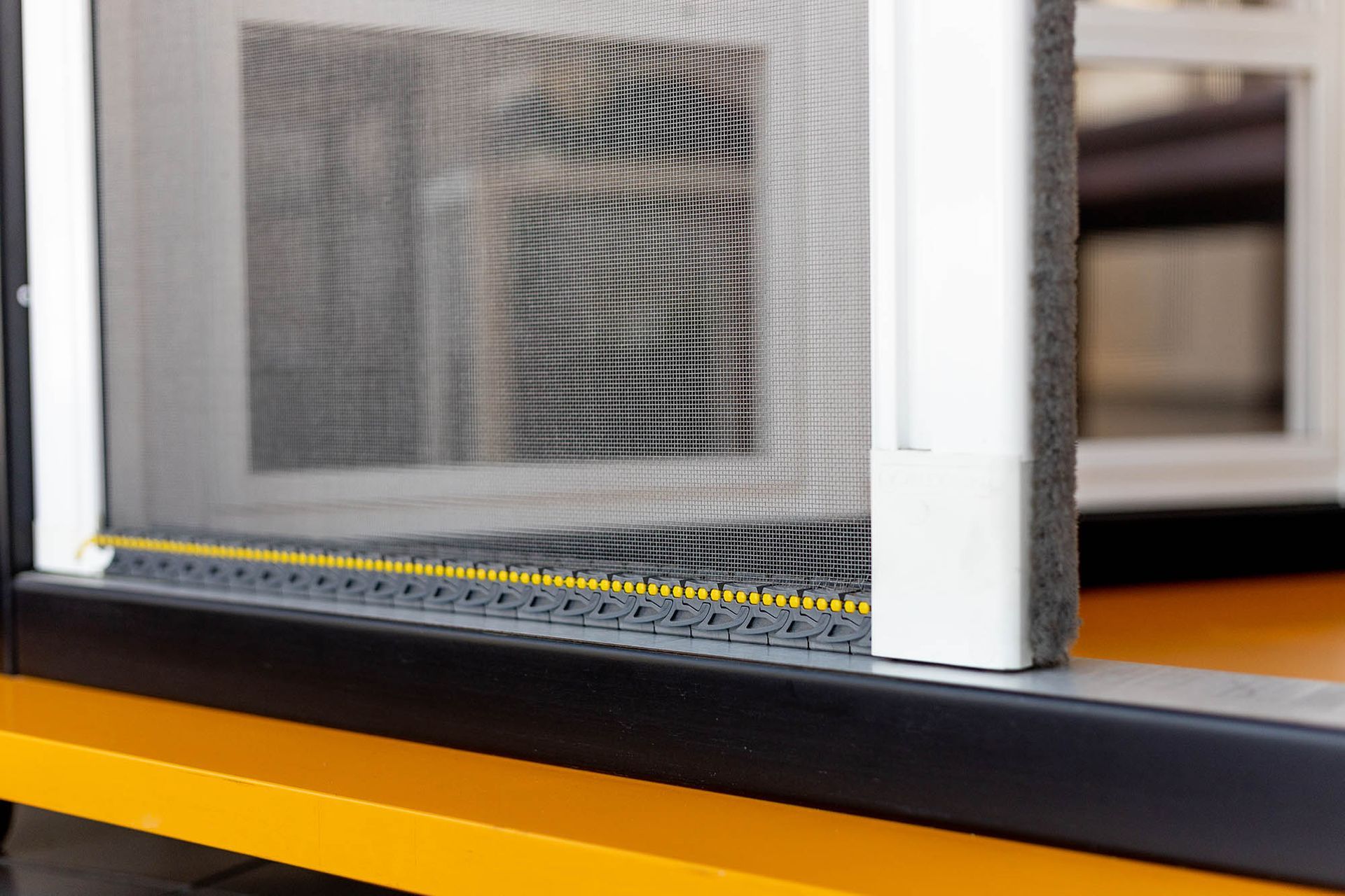Primo piano di una finestra con zanzariera; è a fuoco una cornice gialla e nera.