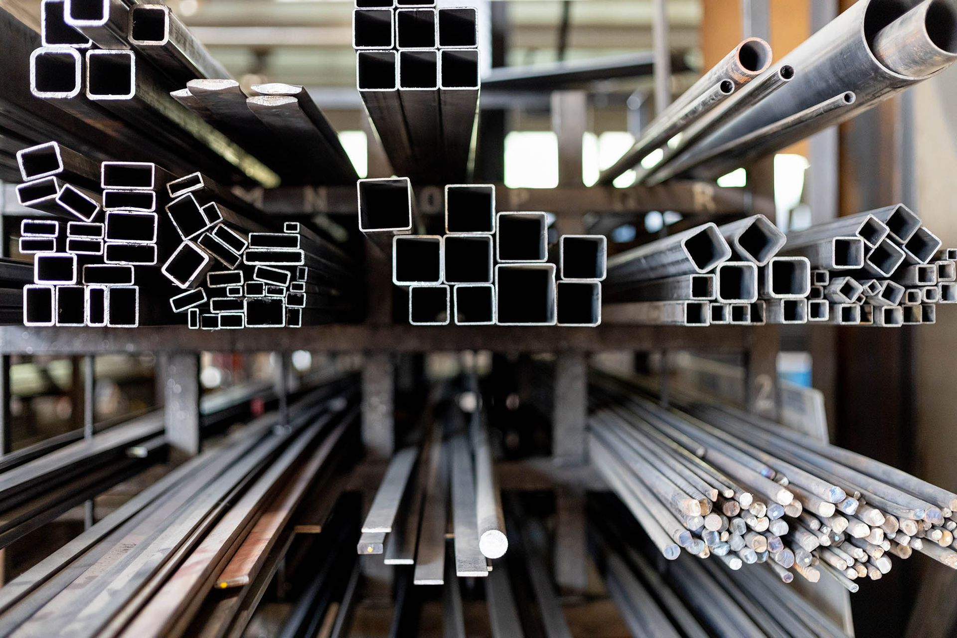 Barre e tubi metallici, disposti su scaffali in un'officina, di varie forme e dimensioni.