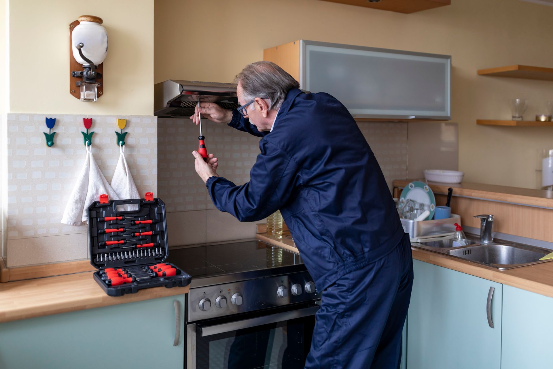 A man is fixing a stove in a kitchen with a screwdriver.