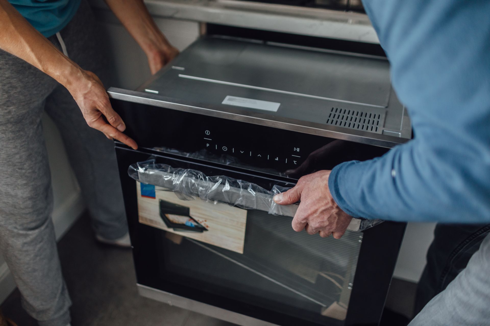 A man and a woman are opening a new oven in a kitchen.