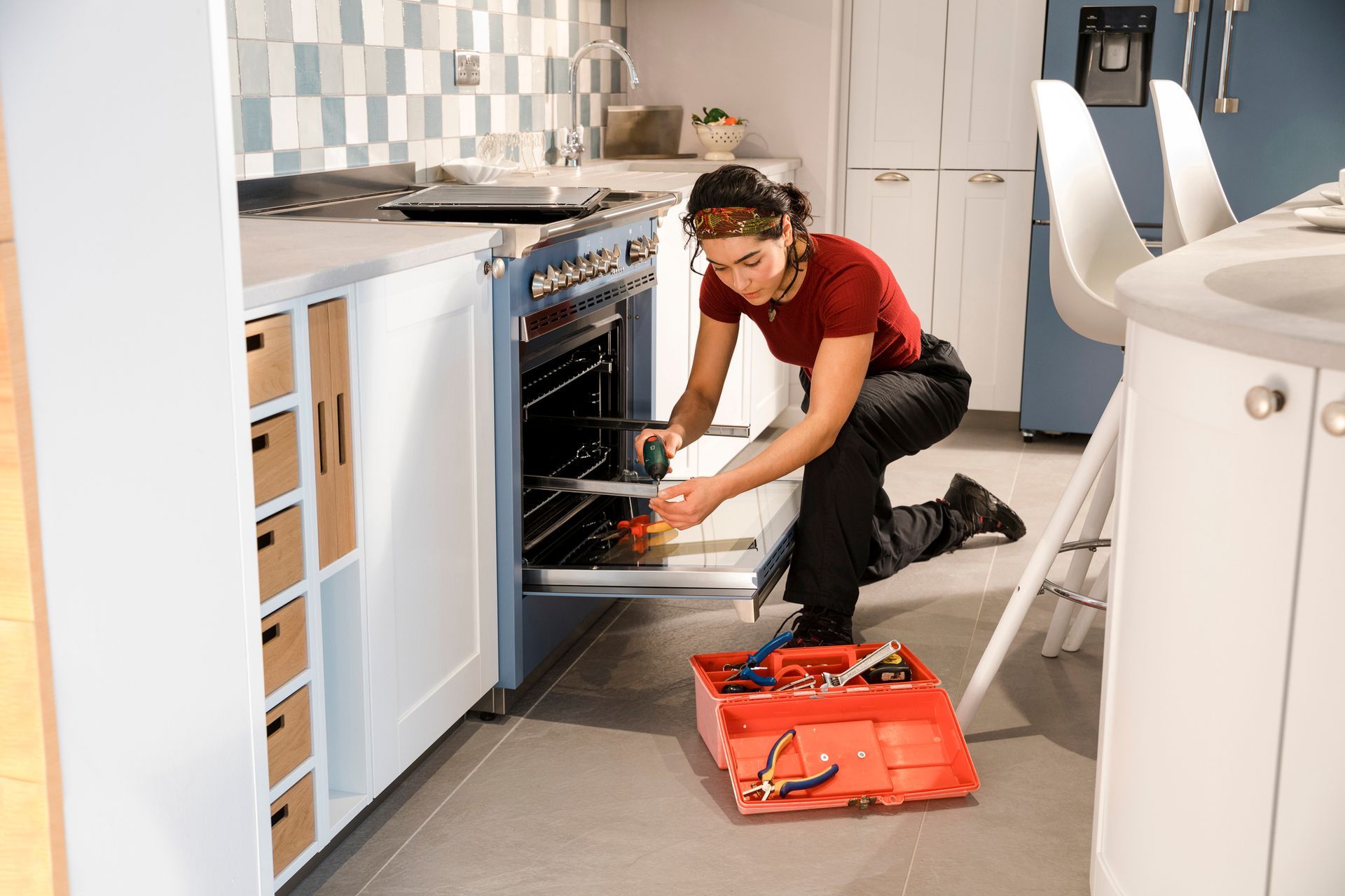 A woman is fixing an oven in a kitchen.