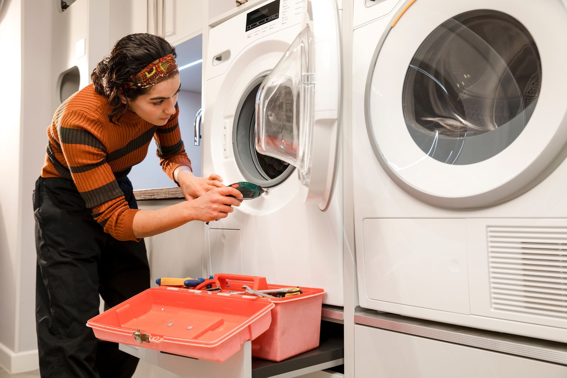 A woman is fixing a washer and dryer in a laundry room.