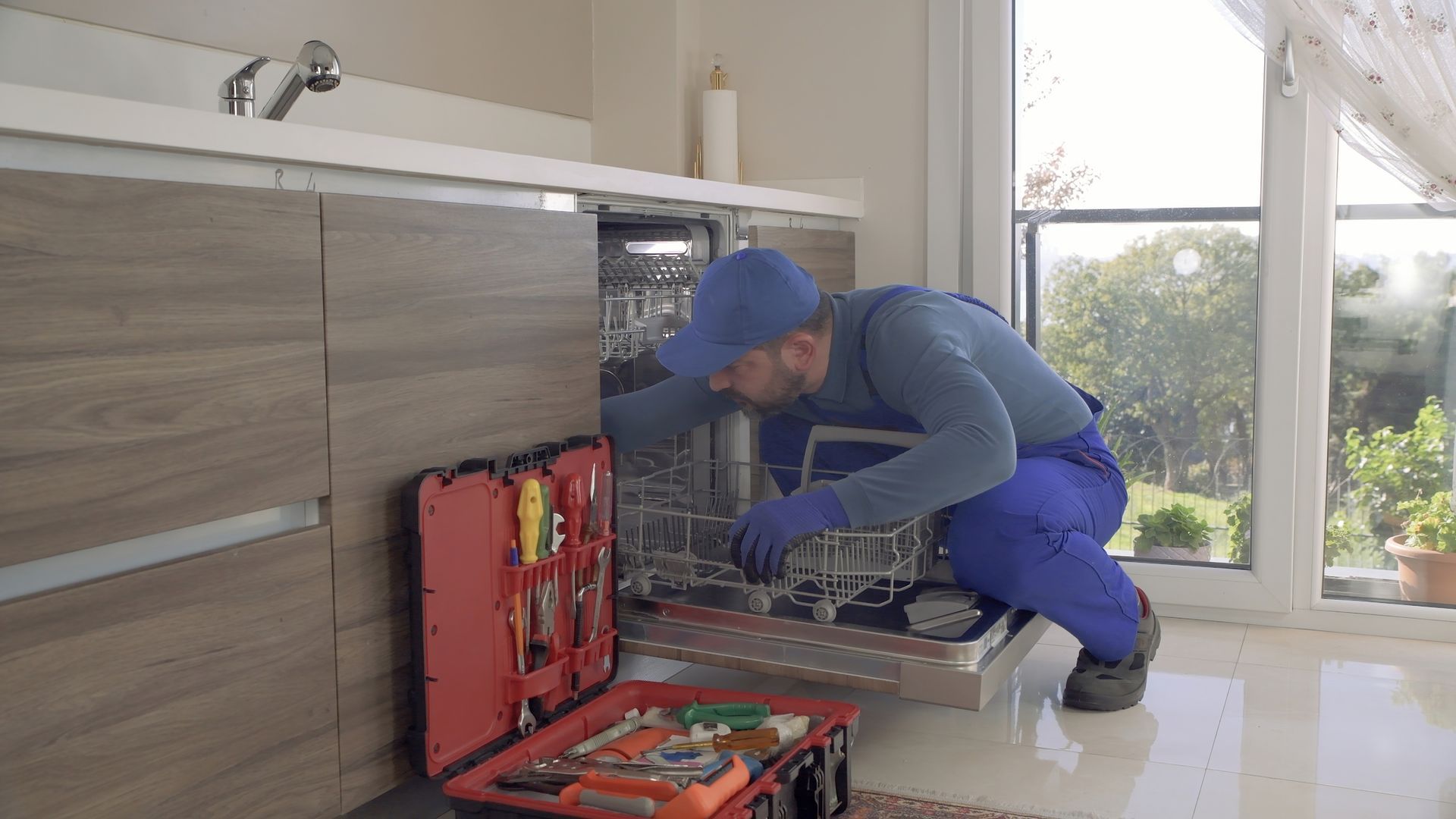 A woman is fixing a dishwasher in a kitchen.