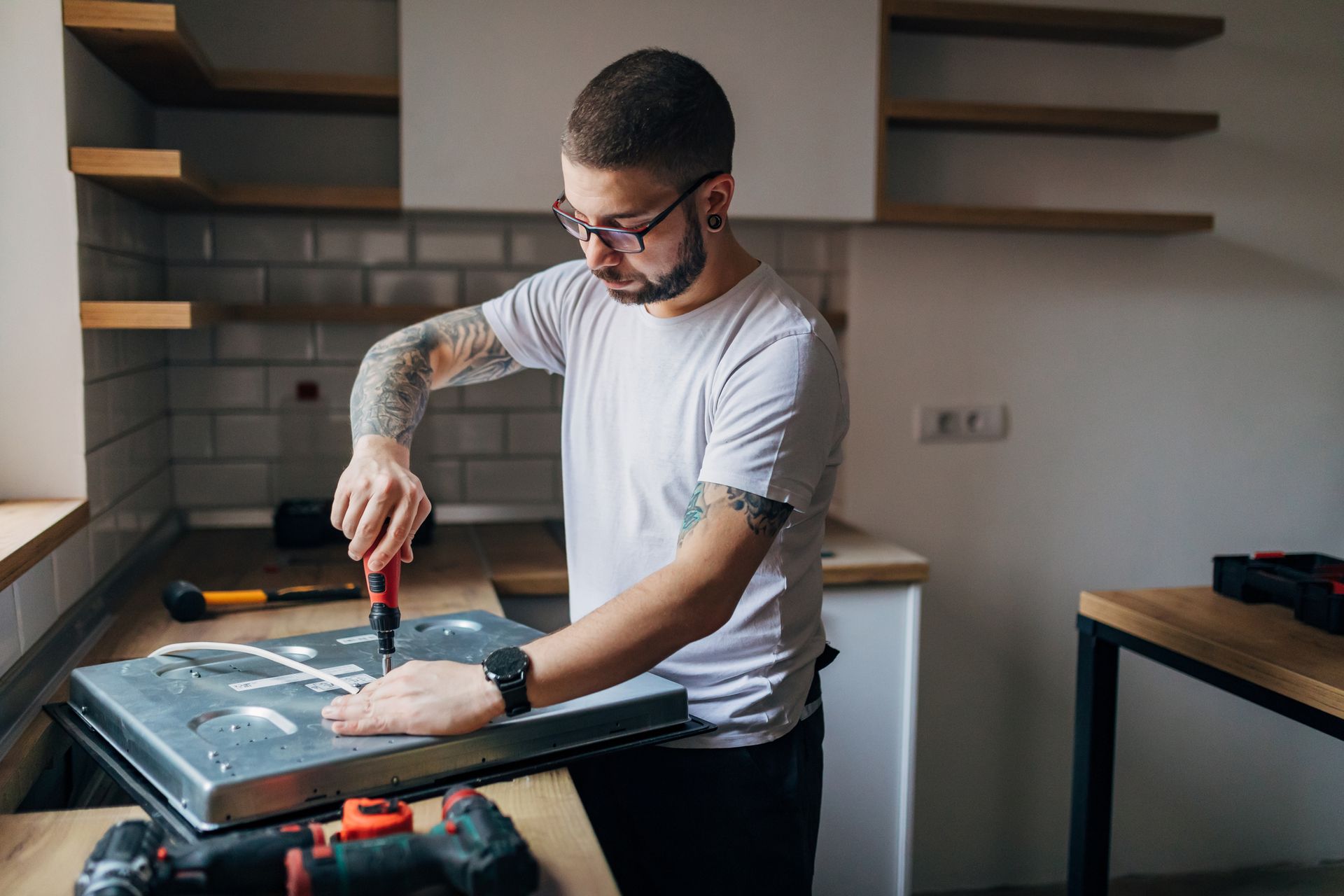 A man is using a drill to fix a stove top in a kitchen.