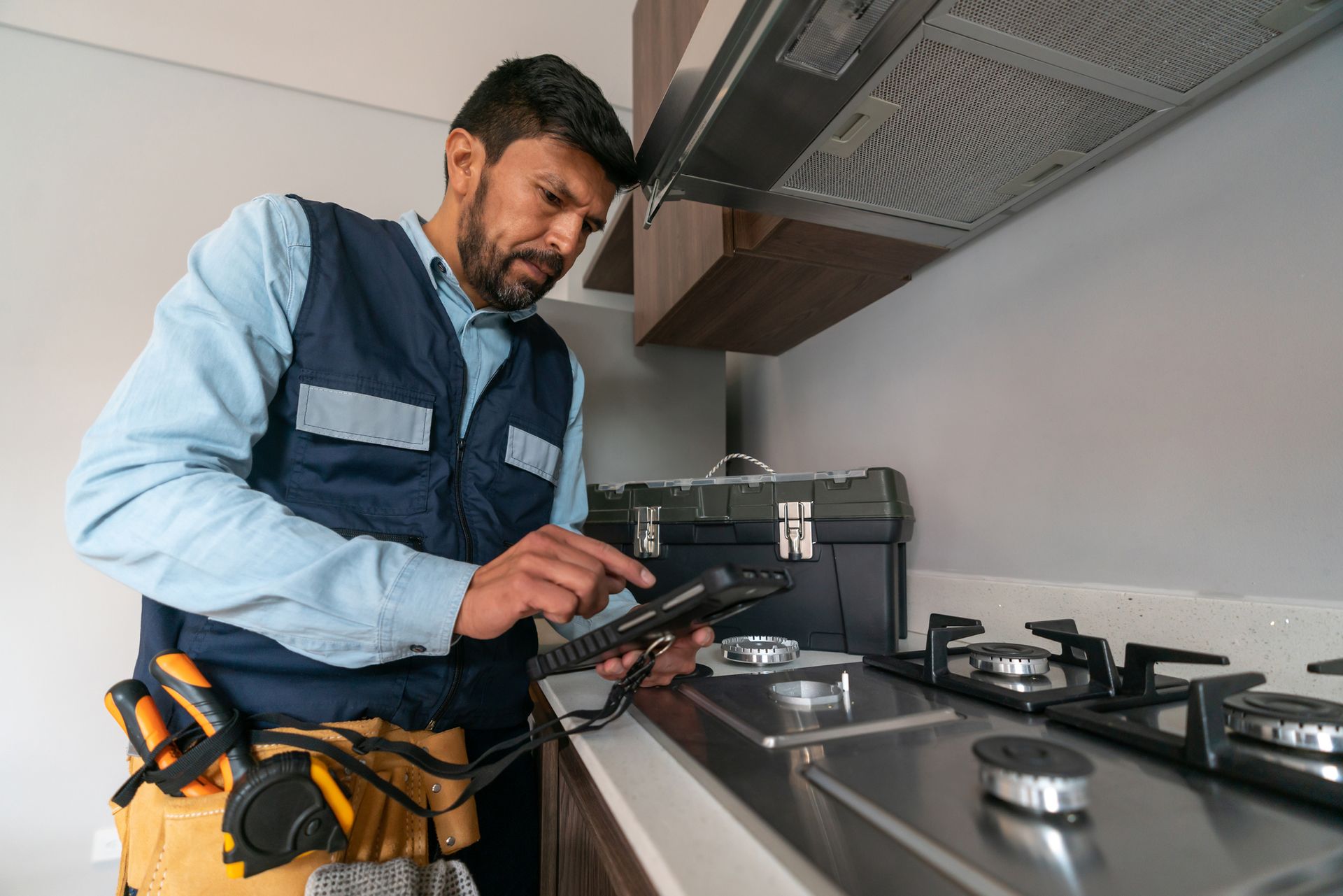 A man is working on a gas stove in a kitchen.