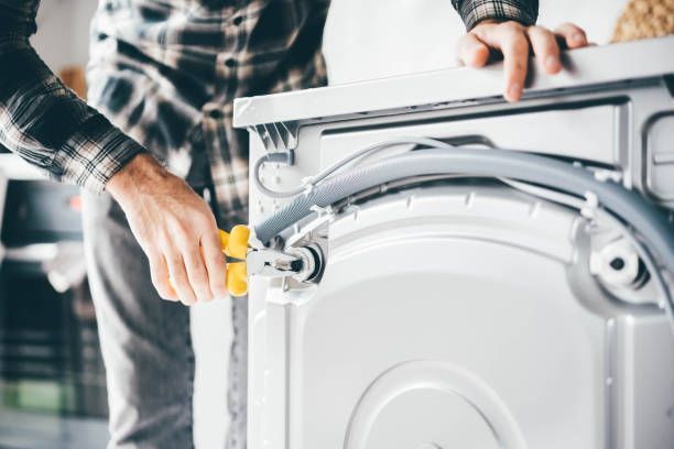 A man is fixing a washing machine with a screwdriver.