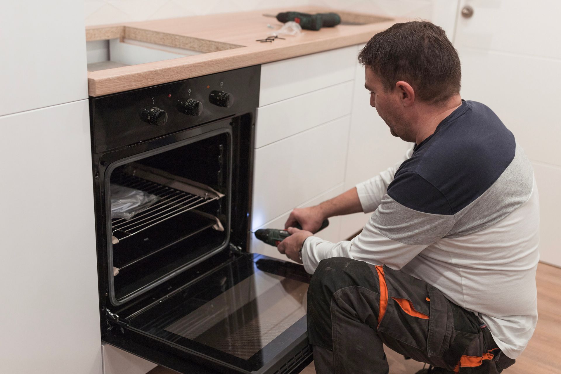 A man is fixing an oven in a kitchen.