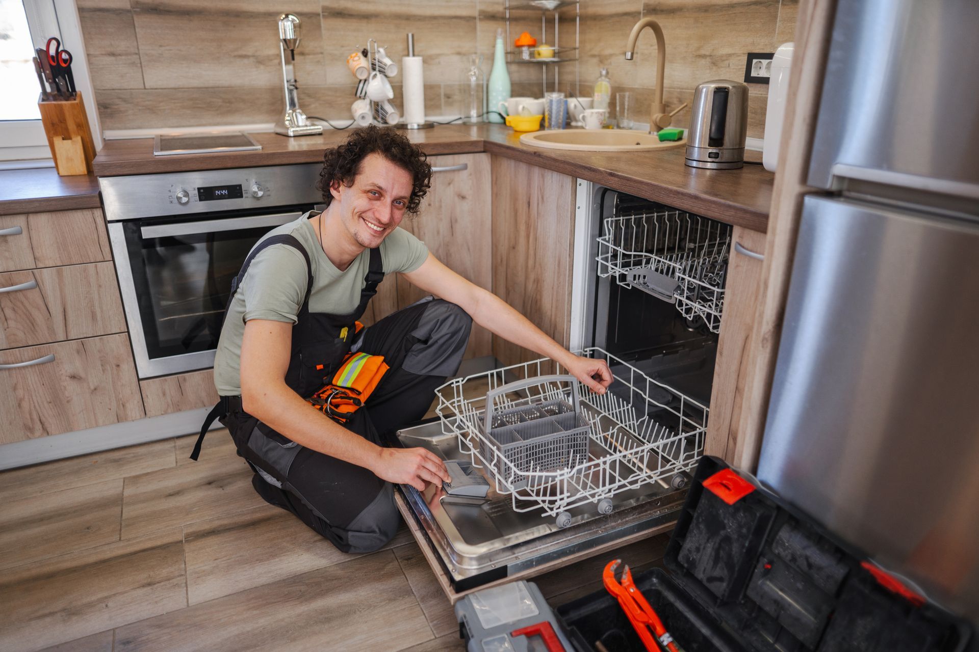A man is kneeling down in a kitchen to fix a dishwasher.