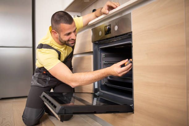 A man is fixing an oven in a kitchen.