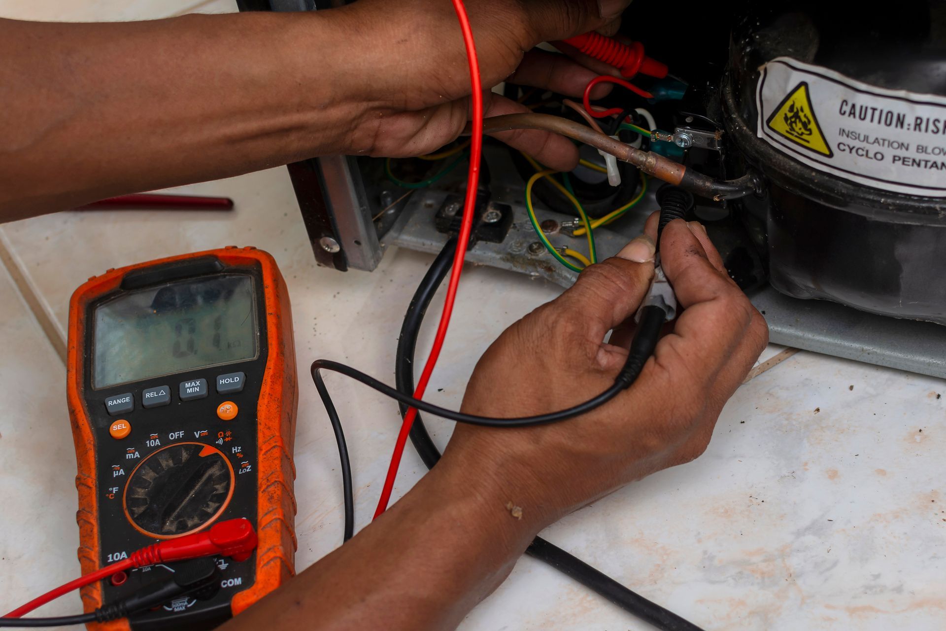 A man is working on a refrigerator with a multimeter next to him
