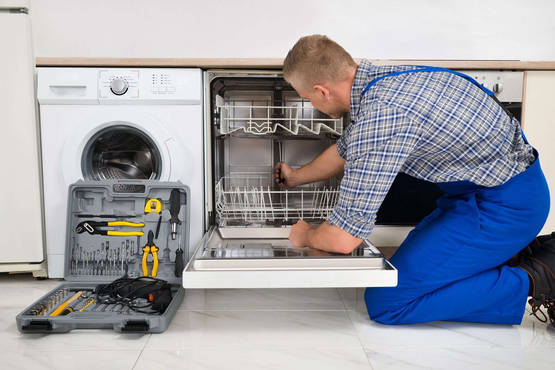 A man is fixing a dishwasher in a kitchen.