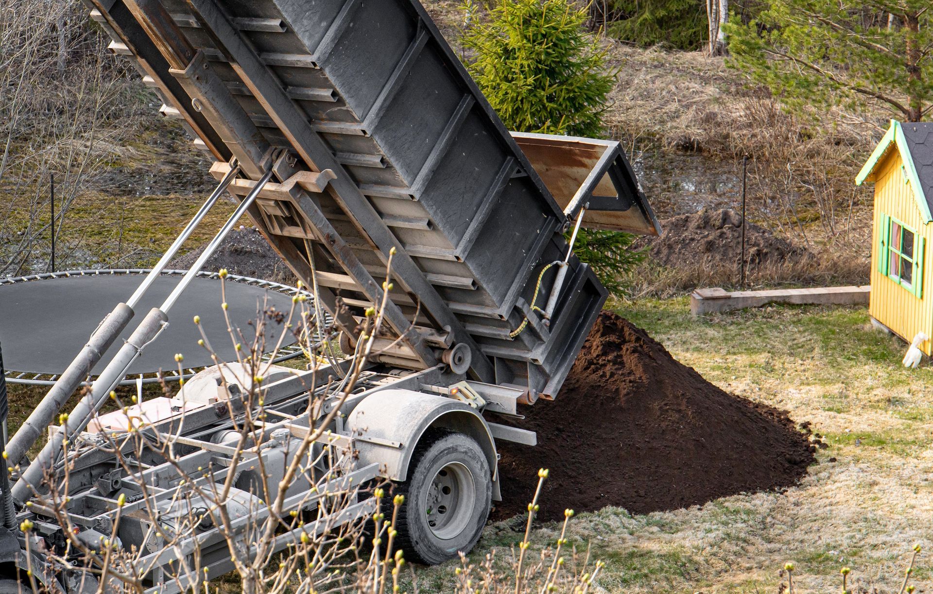 A dump truck is being loaded with dirt in a yard