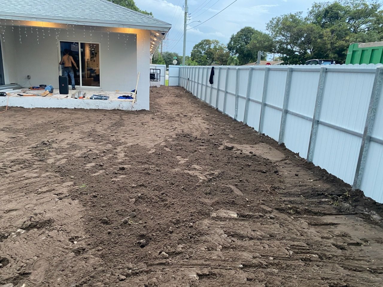 A white fence surrounds a dirt yard in front of a house.