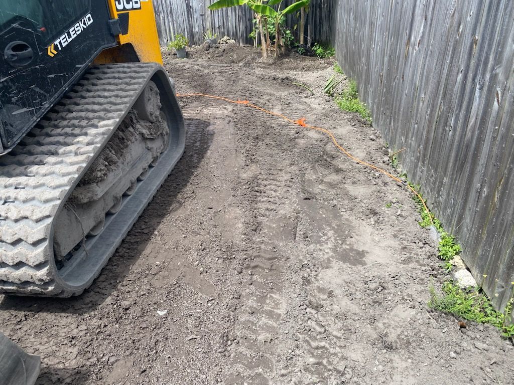 A bulldozer is driving down a dirt road next to a fence.