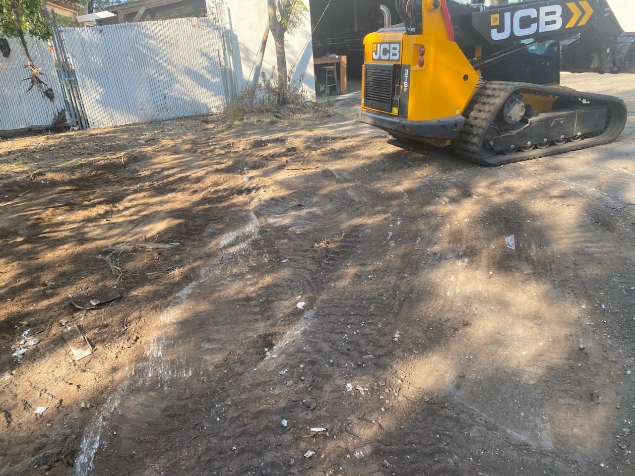 A yellow jcb dump truck is driving down a dirt road.