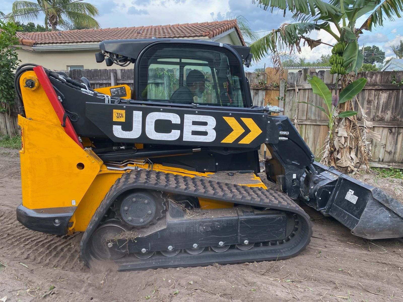 A yellow and black jcb skid steer loader is parked in a dirt lot.