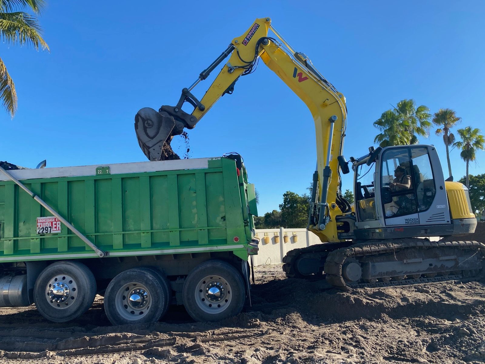 A yellow excavator is loading dirt into a green dump truck.