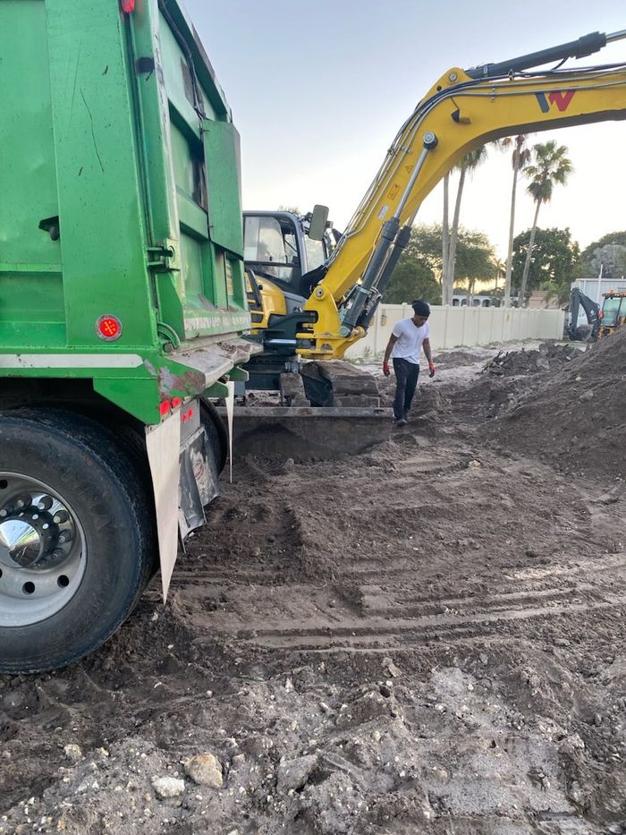 A man is standing next to a dump truck and an excavator.