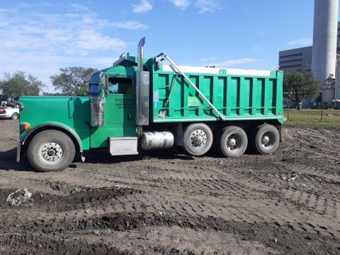 A green dump truck is parked in a dirt field