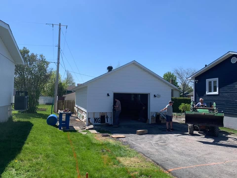 Un homme se tient devant un garage blanc à côté d'une maison noire.