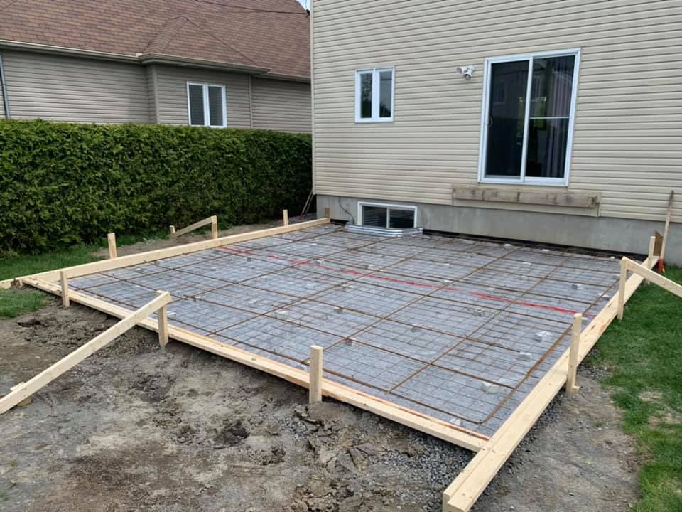 Un patio en béton est en cours de construction devant une maison.