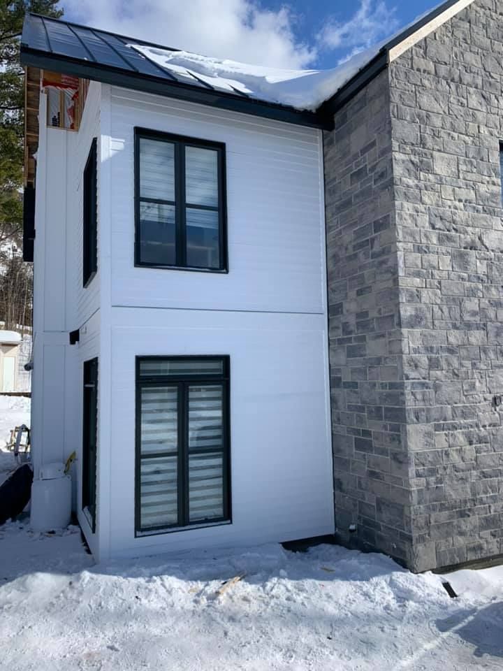 Une maison blanche avec un toit noir est entourée de neige.