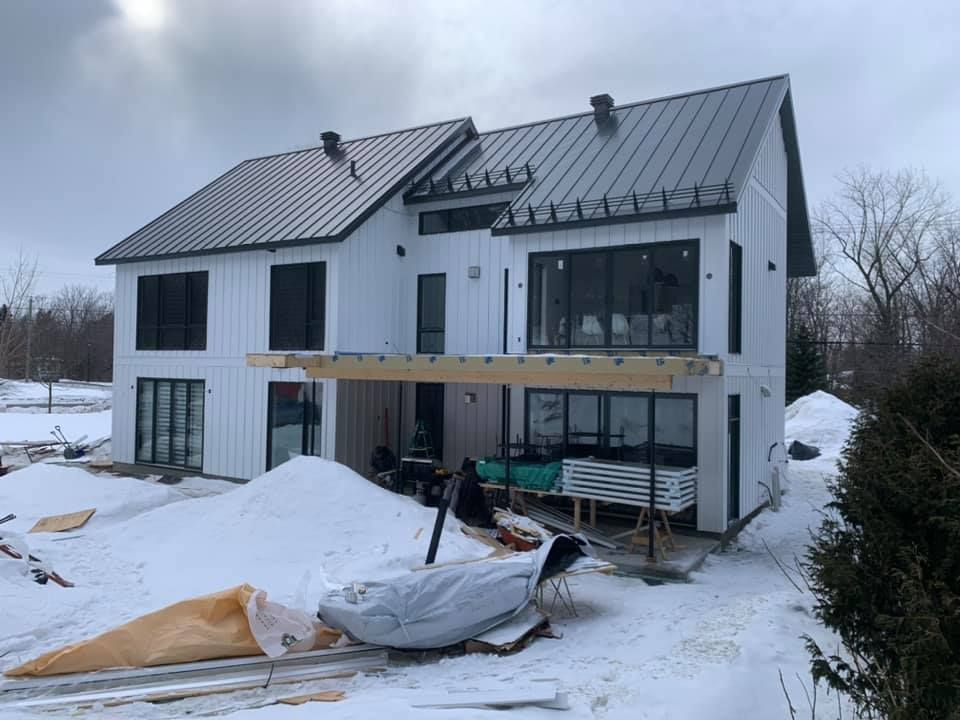 Une grande maison blanche avec un toit noir est en construction dans la neige.
