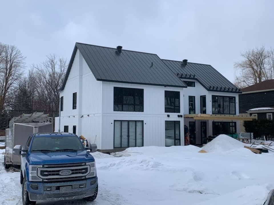 Un camion bleu est garé devant une maison blanche sous la neige.