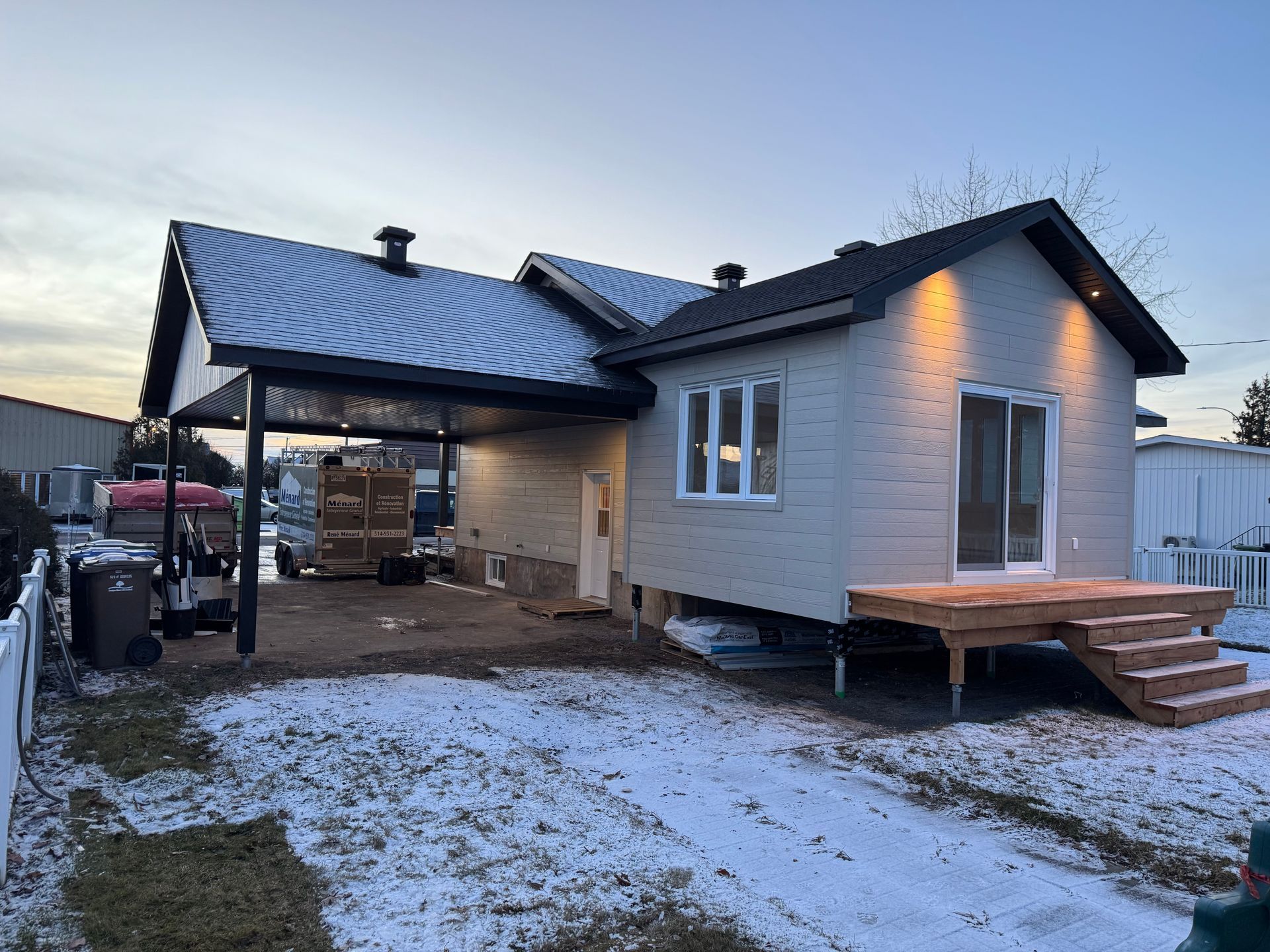 Une petite maison avec un abri voiture et des escaliers est en cours de construction dans la neige.