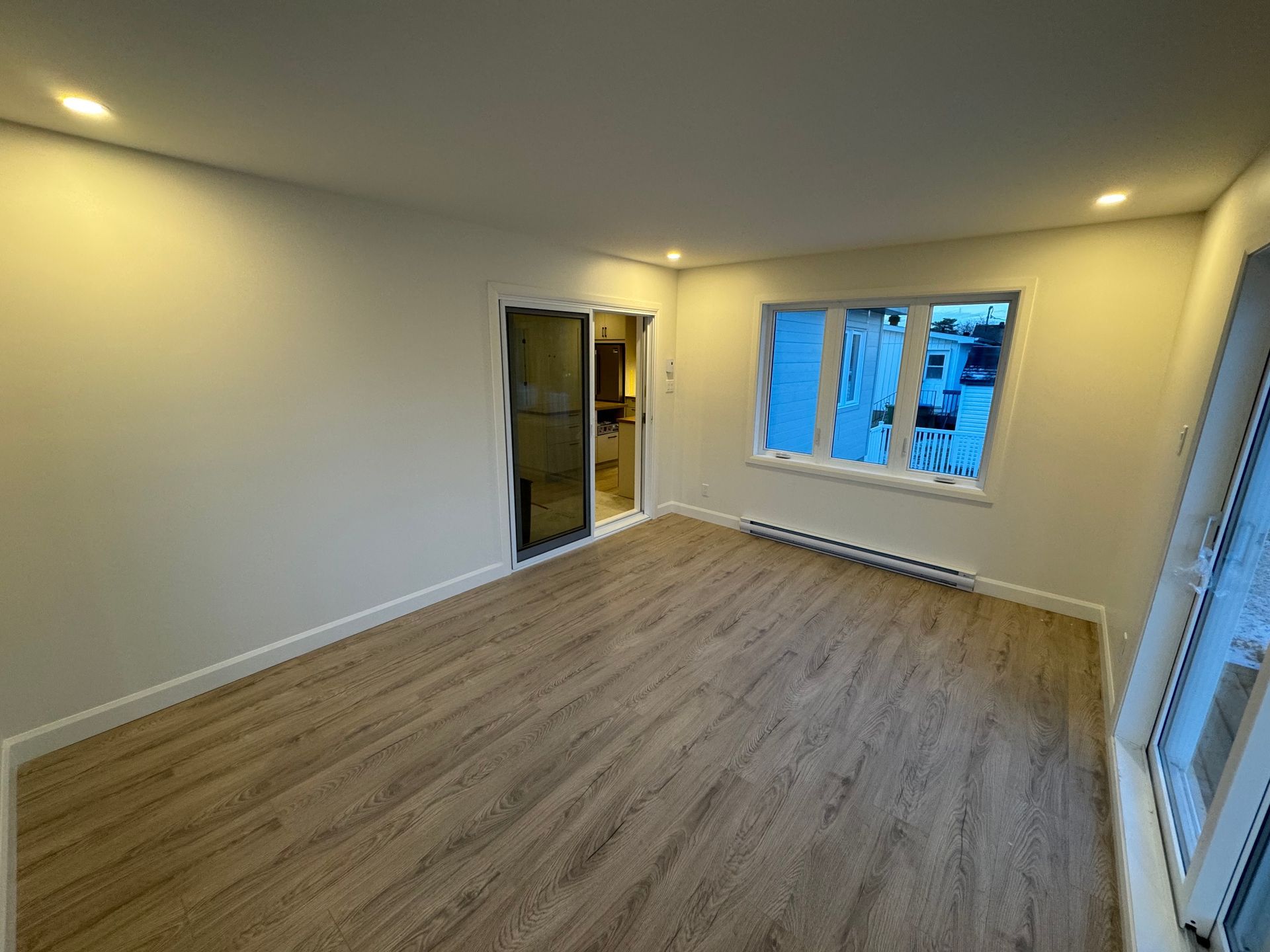 Un salon vide avec parquet et deux fenêtres.