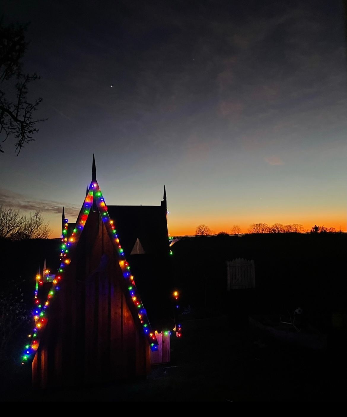træbygning inden solnedgang, med julelys
