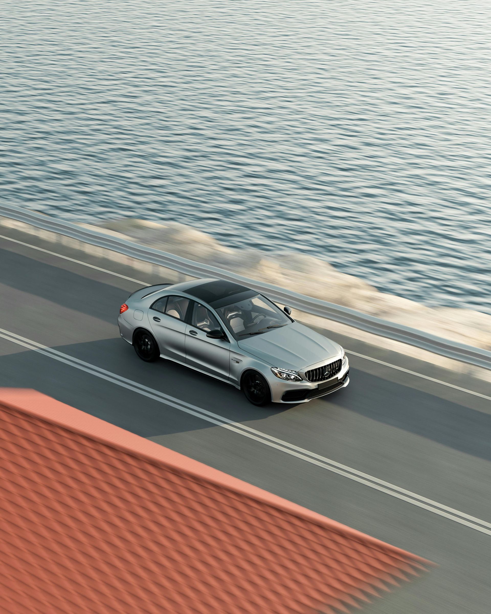 Silver car driving on a road alongside a body of water. Sunny day.